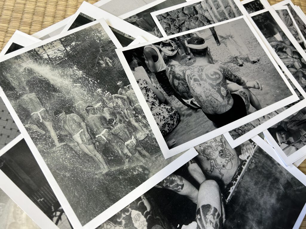 A stack of black and grey fotos depicting tattooed men under a waterfall. One of the pictures shows a man sitting in public. His back and arms covered with tattoos made by Horibun the first. 