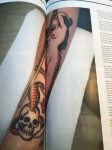 Naked woman with snake and skull tattooed on a forearm