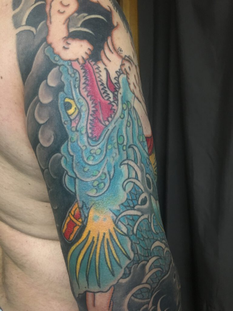 Blue Japanese river monster tattoo on the back of a mans arm.