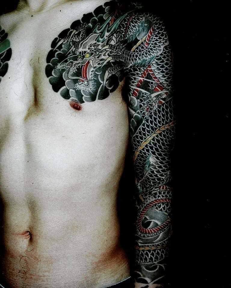 Black Dragon tattooed on mans arm and chest. Open mouth Dragon.