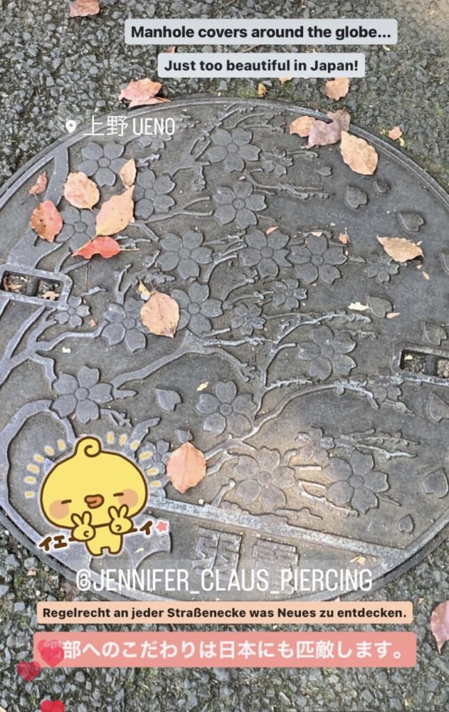 Ueno man hole cover with cherry blossom tree and petals surrounded by tar and other real fallen leaves.