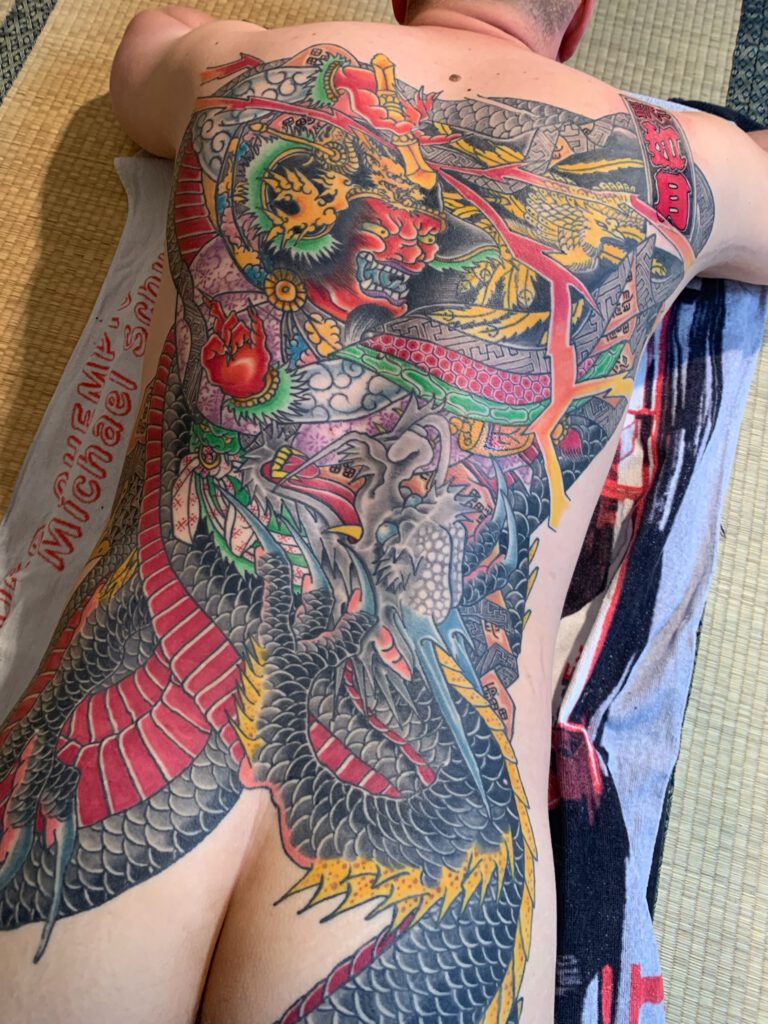 Dragon wrapping the thunder god Rai Tei with many colours. all colours reoccur evenly throughout the work on the mans tattooed back.