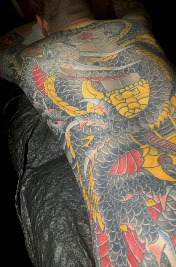 A black dragon winding around a sword over a mans back. Red, Yellow and bits of blue are distributed evenly in the design. Big black blocks make up the background to enhance the image.